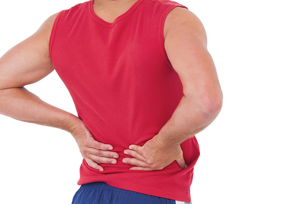 Man in rood hemd houdt met beide handen zijn pijnlijke onderrug vast.