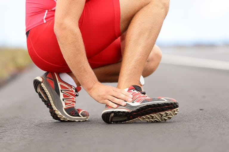 Sporter hurkt neer en houdt enkel vast vanwege pijn of blessure.