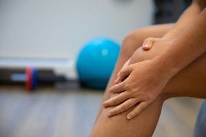 Persoon houdt pijnlijke knie vast in de oefenruimte van de fysiopraktijk.