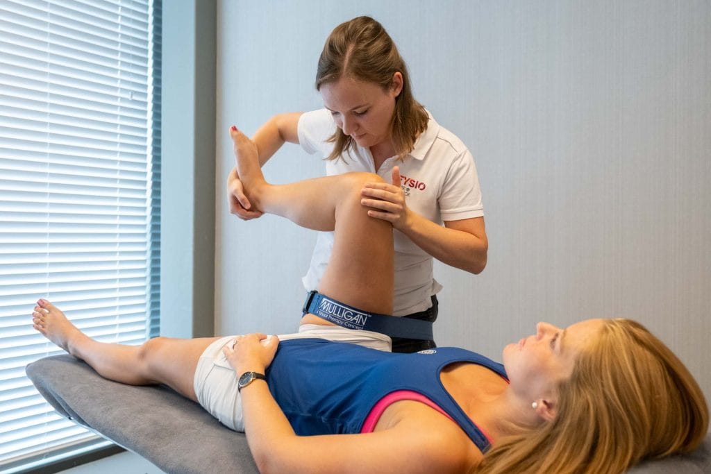 Fysiotherapeute van Fysio Care & Science die een mobilisatietechniek met een Mulligan-band uitvoert bij het been van een cliënte.